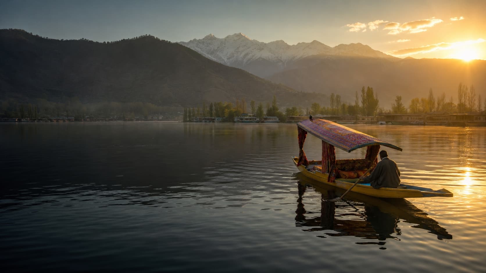A traditional shikara crossing Dal Lake at sunrise beneath Kashmir's mountains